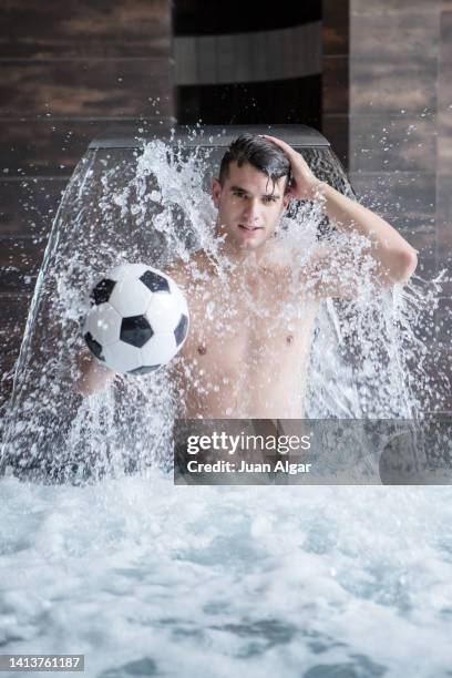 positive young guy standing in pool under waterfall with ball - algar waterfall spain stock pictures, royalty-free photos & images