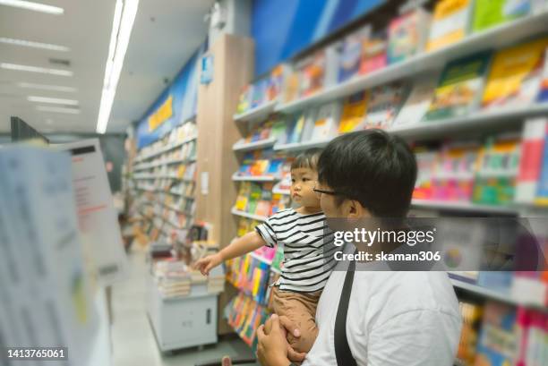 good choice baby asian daddy selecting picture book for daughter baby girl at bookstore - glowing book stock pictures, royalty-free photos & images