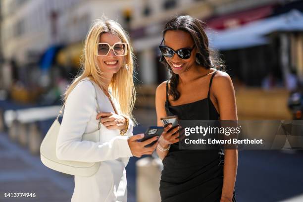 Natalia Verza wears silver earrings, a gold pendants chain short necklace, a white V-neck / long sleeves short dress from Janashia, a white shiny...