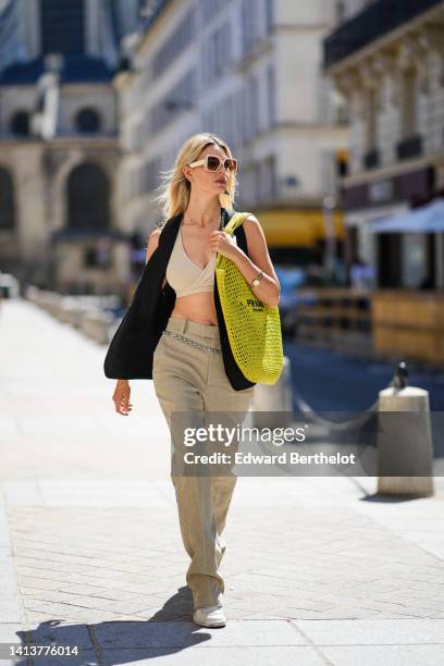 Natalia Verza @mascarada.paris wears white square sunglasses from Louis Vuitton, a silver and black iconic triangular pendant earring from Prada, a...