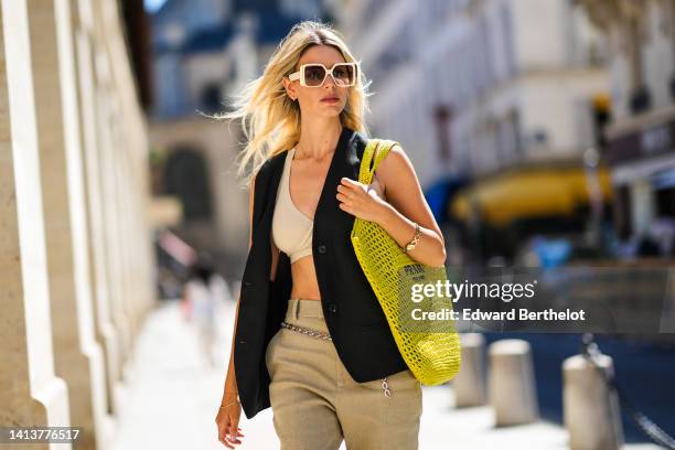 Natalia Verza @mascarada.paris wears white square sunglasses from Louis Vuitton, a silver and black iconic triangular pendant earring from Prada, a...