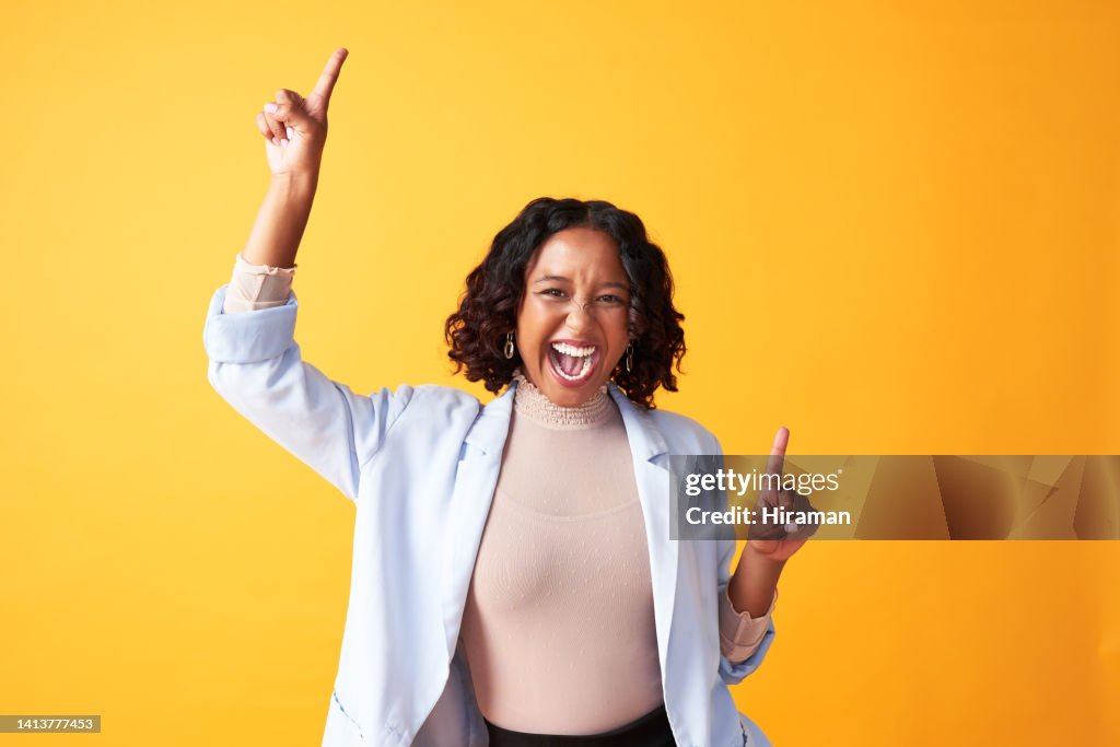 A joyful, cheerful and funny woman dancing against a bright orange background. Portrait of an excited, fun and playful female cheering with fingers pointing up dance. Happy woman doing winner gesture