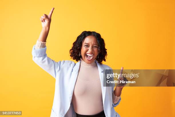 a joyful, cheerful and funny woman dancing against a bright orange background. portrait of an excited, fun and playful female cheering with fingers pointing up dance. happy woman doing winner gesture - excitement stockfoto's en -beelden