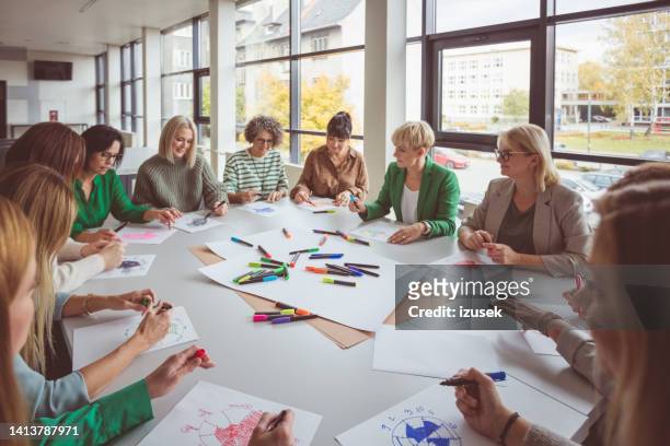 businesswoman talking with team during activity - workshop table stock pictures, royalty-free photos & images