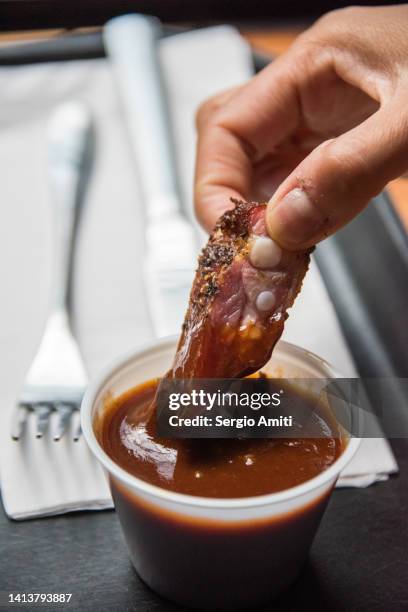 dipping a smoked rib tip in bbq sauce - salsa barbecue foto e immagini stock