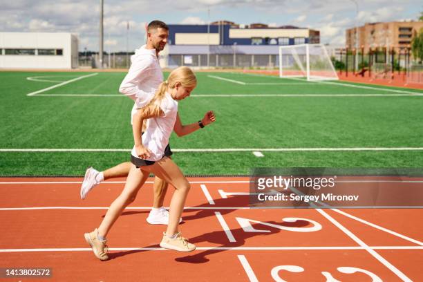 father with daughter together running on track and field stadium - running coach stock pictures, royalty-free photos & images