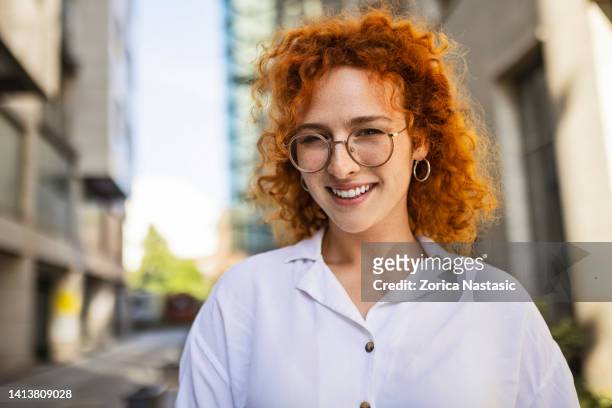 une jeune femme d’affaires se tient devant un immeuble de bureaux en regardant la caméra - cats eye glasses photos et images de collection