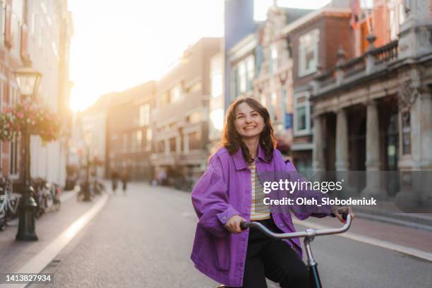 woman riding bicycle in the city at sunset - vrouw fiets stockfoto's en -beelden