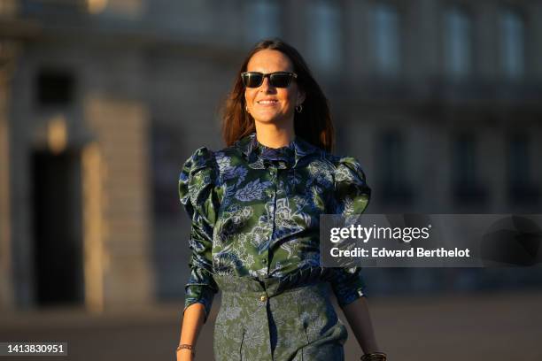 Alba Garavito Torre wears black sunglasses from Ray Ban, gold earrings, a dark green and blue gray flower print pattern puffy shoulder / long sleeves...