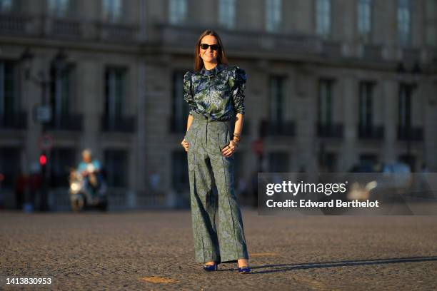 Alba Garavito Torre wears black sunglasses from Ray Ban, gold earrings, a dark green and blue gray flower print pattern puffy shoulder / long sleeves...