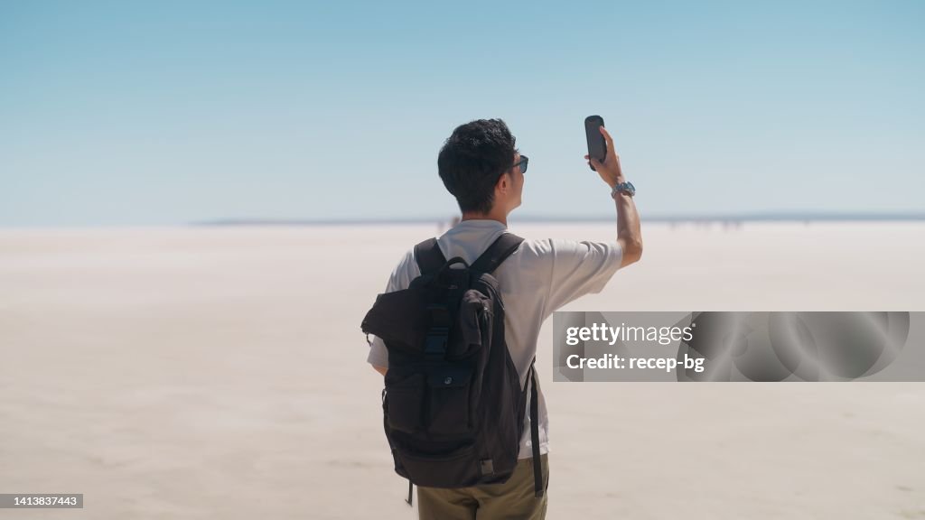 ソルトレークの白い塩で携帯電話でビデオや写真を撮っている若い男性観光客