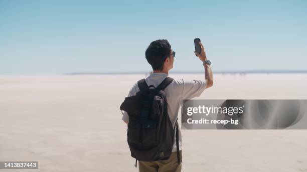 young male tourist taking videos and photos with his mobile phone on white salt in salt lake - 360 people stock pictures, royalty-free photos & images