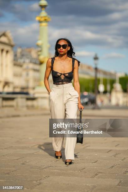 Emilie Joseph @in_fashionwetrust wears black sunglasses, diamonds earrings, a black lace flower pattern corset top, high waist beige wide legs pants...