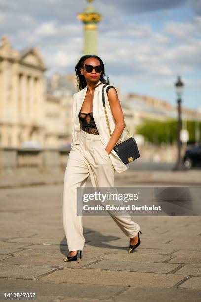 Emilie Joseph @in_fashionwetrust wears black sunglasses, diamonds earrings, a black lace flower pattern corset top, high waist beige wide legs pants...