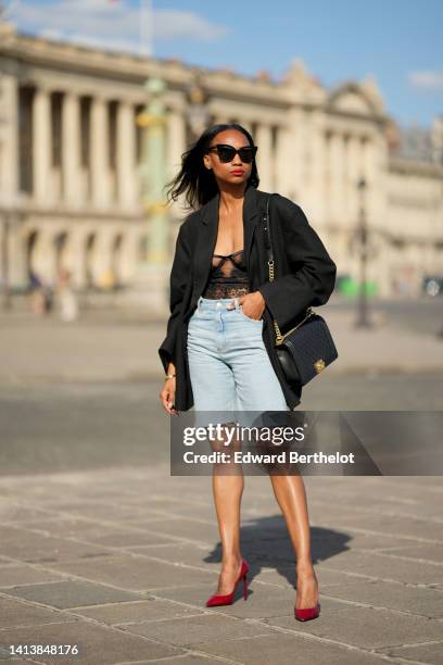 Emilie Joseph @in_fashionwetrust wears black sunglasses, diamonds earrings, a black flower print pattern lace corset top, a black oversized blazer...