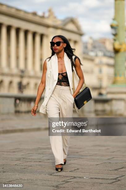 Emilie Joseph @in_fashionwetrust wears black sunglasses, diamonds earrings, a black lace flower pattern corset top, high waist beige wide legs pants...