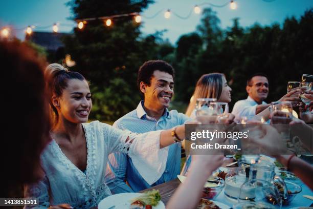 multi-ethnic group of people eating in the backyard in summer evening and having fun - outdoor dining stock pictures, royalty-free photos & images