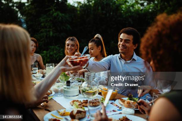 multi-ethnic group of people eating in the backyard in summer evening and having fun - black couple dining stockfoto's en -beelden