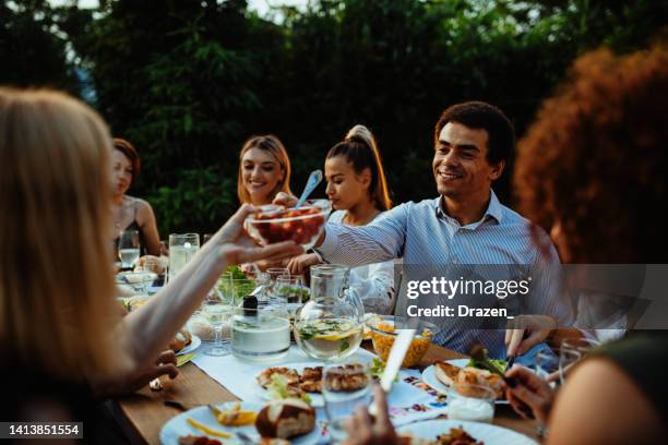 multi-ethnic group of people eating in the backyard in summer evening and having fun - outdoor dining stock pictures, royalty-free photos & images