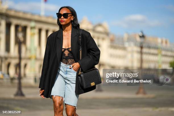 Emilie Joseph @in_fashionwetrust wears black sunglasses, diamonds earrings, a black flower print pattern lace corset top, a black oversized blazer...