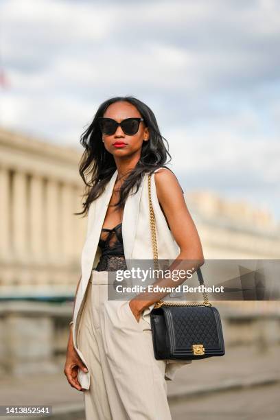 Emilie Joseph @in_fashionwetrust wears black sunglasses, diamonds earrings, a black lace flower pattern corset top, high waist beige wide legs pants...