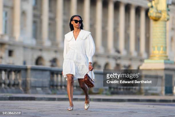 Emilie Joseph wears black sunglasses, diamond earrings, a white summer shirt Dress in cotton poplin with a V-neck / wide rounded peterpan collar /...