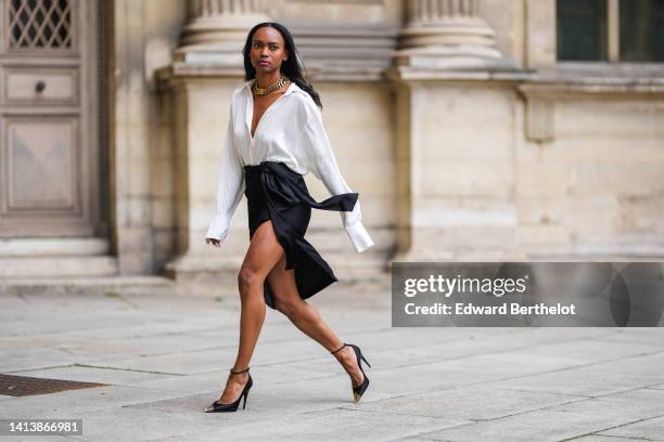 Emilie Joseph @in_fashionwetrust wears golden thick chain necklaces by Merbabe Greece, a white wrap silk shirt, a black silk wrap / slit knees skirt,...