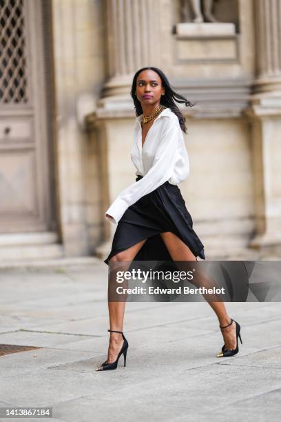 Emilie Joseph @in_fashionwetrust wears golden thick chain necklaces by Merbabe Greece, a white wrap silk shirt, a black silk wrap / slit knees skirt,...