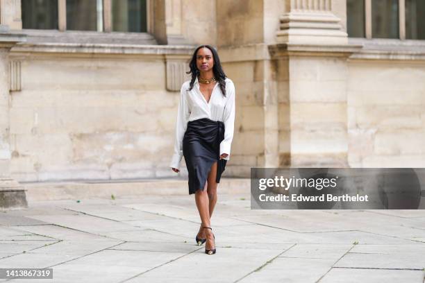 Emilie Joseph @in_fashionwetrust wears golden thick chain necklaces by Merbabe Greece, a white wrap silk shirt, a black silk wrap / slit knees skirt,...