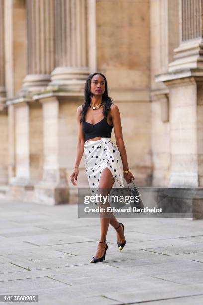 Emilie Joseph @in_fashionwetrust wears a large golden thick chain by Merbabe Greece, a black ribbed V-neck / cropped tank-top, gold bracelets, a...