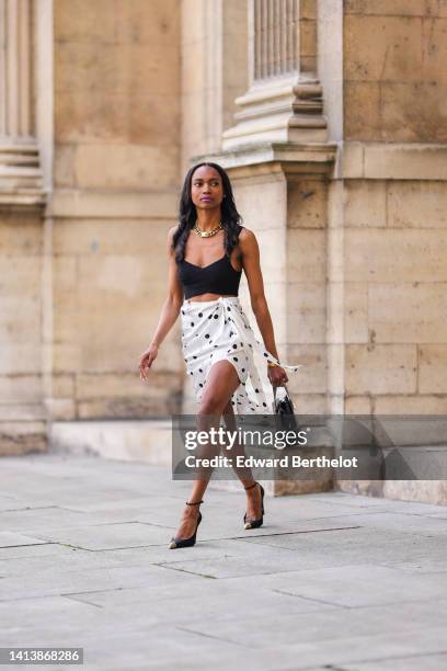Emilie Joseph @in_fashionwetrust wears a large golden thick chain by Merbabe Greece, a black ribbed V-neck / cropped tank-top, gold bracelets, a...