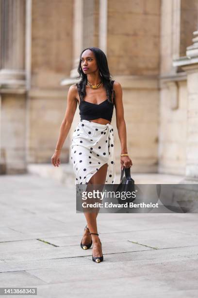 Emilie Joseph @in_fashionwetrust wears a large golden thick chain by Merbabe Greece, a black ribbed V-neck / cropped tank-top, gold bracelets, a...