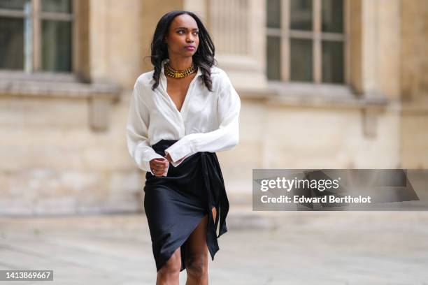 Emilie Joseph @in_fashionwetrust wears golden thick chain necklaces by Merbabe Greece, a white wrap silk shirt, a black silk wrap / slit knees skirt,...