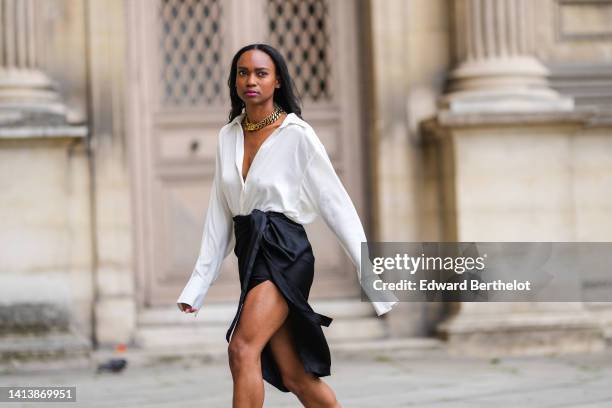 Emilie Joseph @in_fashionwetrust wears golden thick chain necklaces by Merbabe Greece, a white wrap silk shirt, a black silk wrap / slit knees skirt,...