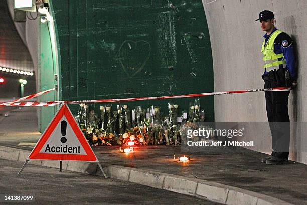Police officer stands next to floral tributes and candles laid by the families at the scene in the road tunnel where the 22 Belgian school children,...
