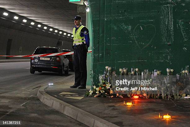 Police officer stands next to floral tributes laid by the families at the scene in the road tunnel where the 22 Belgian school children, four...