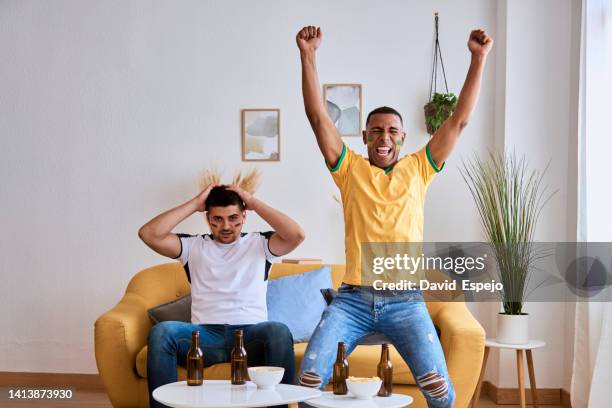 excited young man celebrating a goal while watching a world cup soccer match with a friend. - championship round two stockfoto's en -beelden