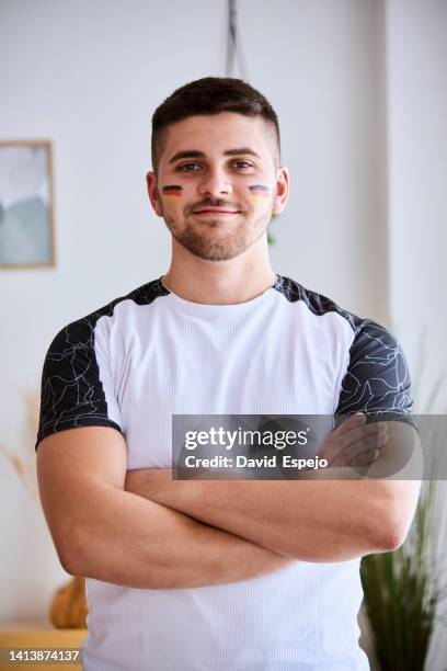 man looking at camera while posing wearing a sports t-shirt and with the germany flag painted on cheek. - pittura per il viso foto e immagini stock