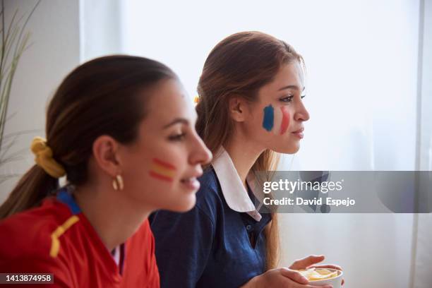 women supporting the spanish and french soccer teams while watching a world cup match together. - french cup soccer stock pictures, royalty-free photos & images