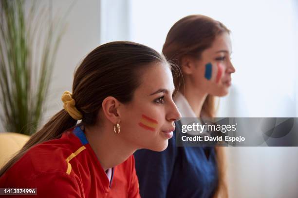 women supporting the spanish and french soccer teams while watching a world cup match together. - french cup soccer stock pictures, royalty-free photos & images