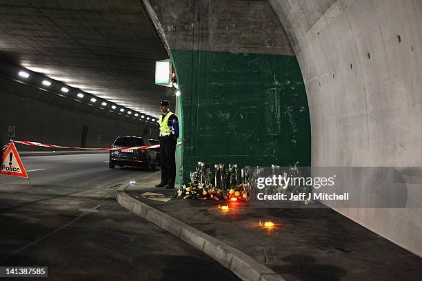 Police officer stands next to floral tributes laid by the families at the scene in the road tunnel where the 22 Belgian school children, four...