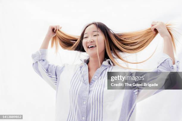 cheerful young woman with eyes closed playing with hair - mèche foto e immagini stock