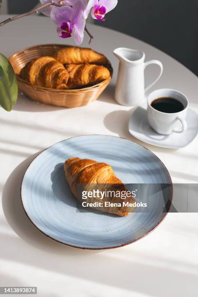 fresh and fragrant croissants in a wicker basket on the table on a bright sunny morning. - coffee cup light stock pictures, royalty-free photos & images