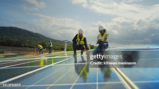 Team-Auftragnehmer, männlicher Ingenieur und weibliche Techniker, die Sicherheitsuniform tragen, über den Installationsplan sprechen, das Arbeitssystem überprüfen und das Solarpanel des Solarkraftwerks warten, um Strom auf dem Dach des Fabrikgebäudes Team-Auftragnehmer, männlicher Ingenieur und weibliche Techniker, die Sicherheitsuniform tragen, über den Installationsplan sprechen, das Arbeitssystem überprüfen und das Solarpanel des Solarkraftwerks warten, um Strom auf dem Dach des Fabrikgebäudes