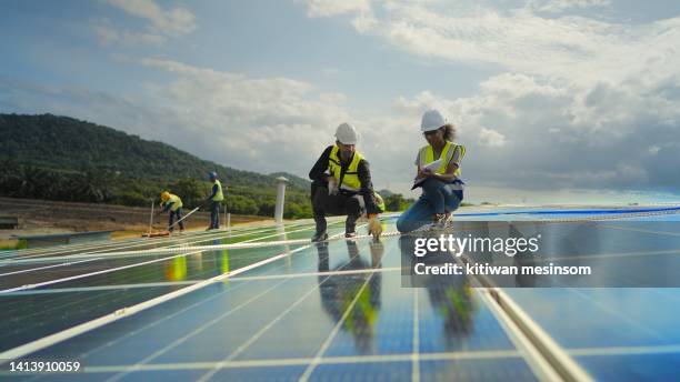 team contractor, male engineer and female technicians  wearing safety uniform, talking about installing plan, check the working system and maintenance solar panel of solar power plant to produce electricity on the roof of factory building. - electrical safety stock pictures, royalty-free photos & images