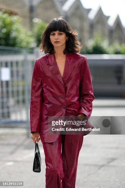 Guest wears a red / burgundy leather jacket, matching pants, a black leather crocodile pattern bag, outside Gestuz, during Copenhagen Fashion Week...