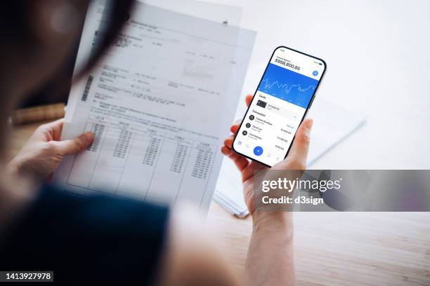 over the shoulder view of young asian woman using online banking app on smartphone, checking financial bills, calculate expenses and pays tax online at home. wealth management. electronic banking. digital banking habits. smart banking with technology - stress test stockfoto's en -beelden