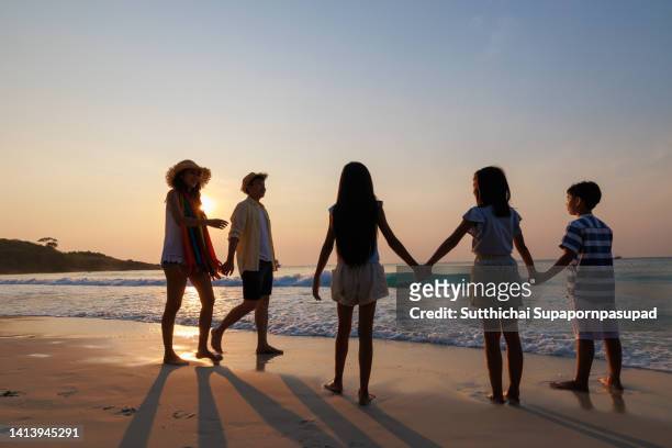 asian parent with three children holding hand together on the beach during sunset. - child silhouette ocean stock pictures, royalty-free photos & images