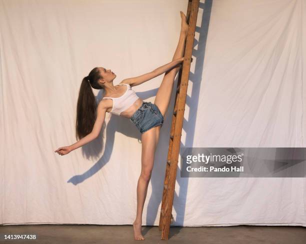 young pretty brunette teenage girl doing splits while standing by a wooden ladder - women in harmony stock pictures, royalty-free photos & images