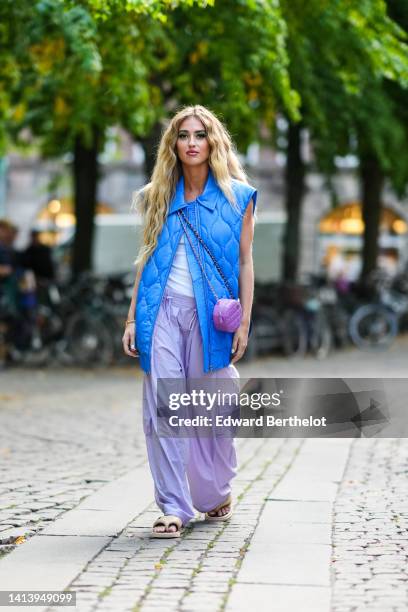 Emili Sindlev wears a royal blue quilted / sleeveless / oversized zipper gilet, a white sleeveless t-shirt, pale purple large cargo pants, a purple...